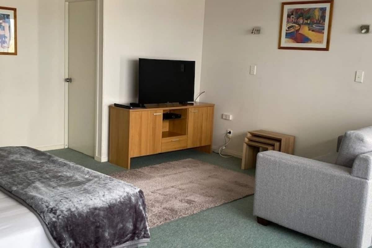 A room with a bed, a grey sofa, a wooden TV stand, and a small table.
