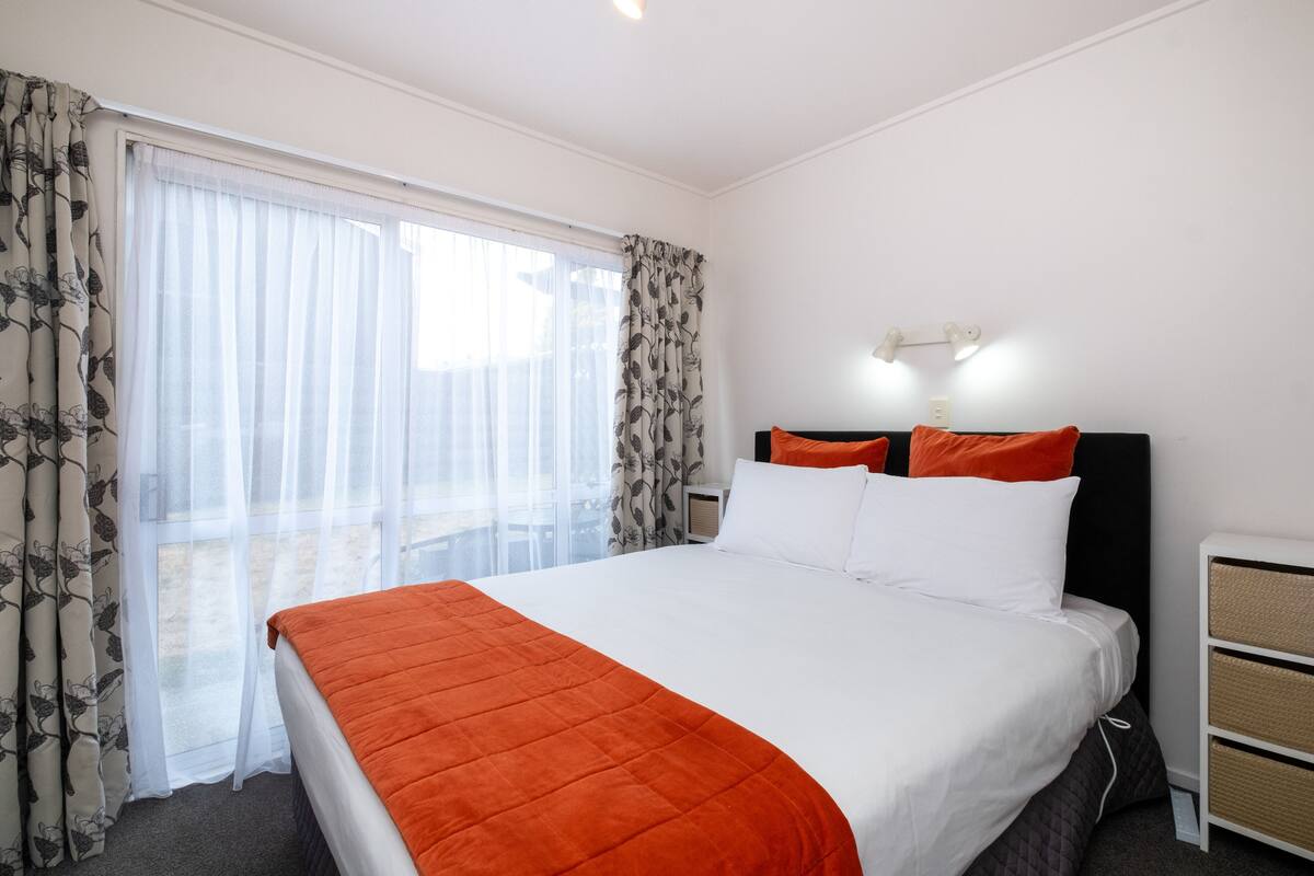 A hotel room with a large bed, white bedding, and a view through sheer curtains.