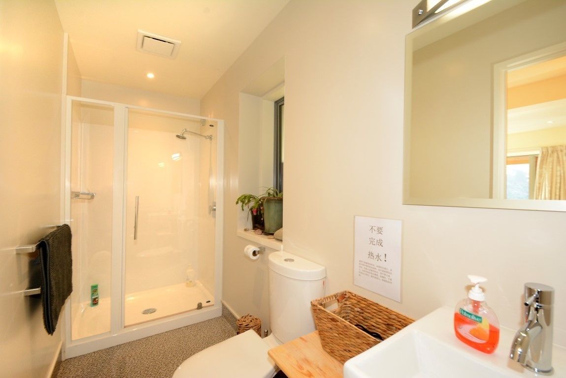 A modern bathroom with a glass-enclosed shower, a toilet, a sink with a mirror, and a small shelf with toiletries.