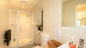 A modern bathroom with a glass-enclosed shower, a toilet, a sink with a mirror, and a small shelf with toiletries.