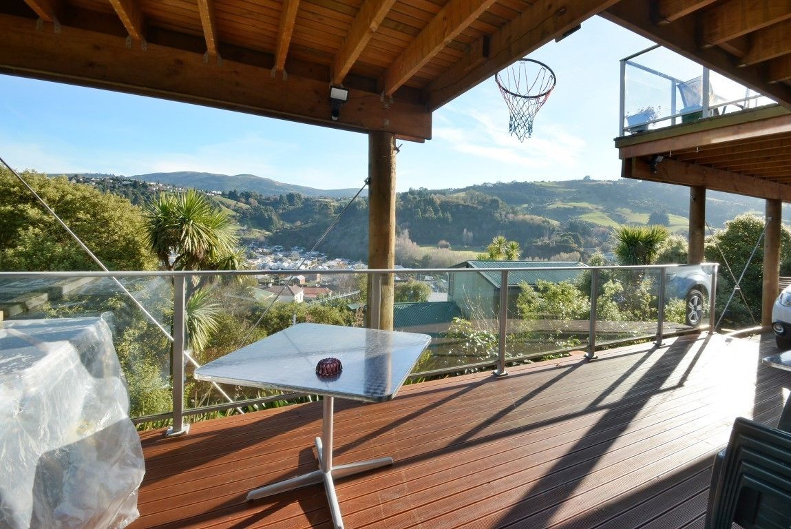 A wooden deck with a glass balustrade overlooking a valley with houses and greenery.