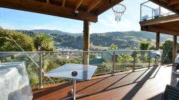 A wooden deck with a glass balustrade overlooking a valley with houses and greenery.