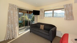 A room with a sofa, a TV, and a view through a glass door. - Baldwin Street BNB (Dunedin)
