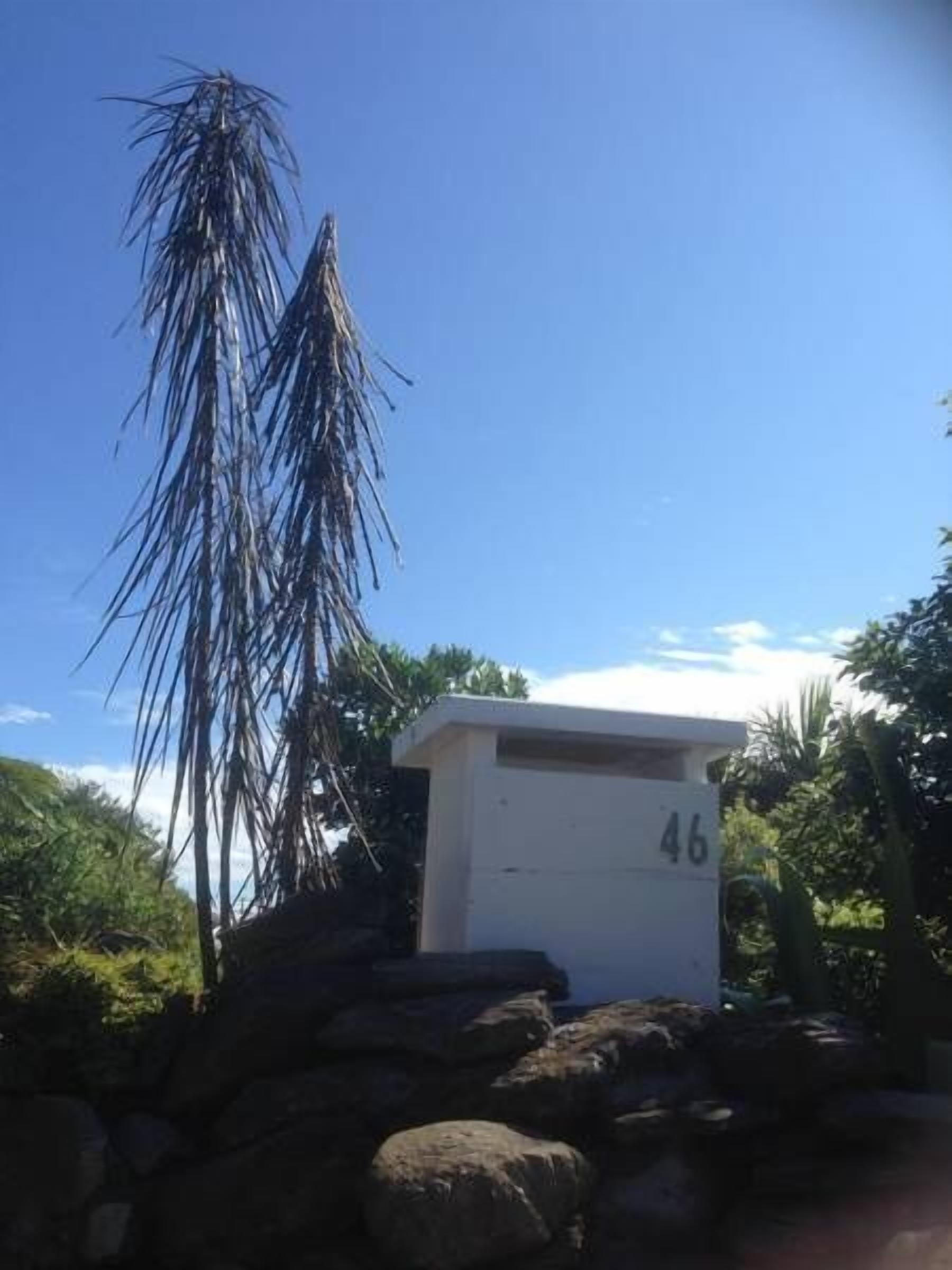 A small white building with the number 46 on it, surrounded by rocks and vegetation.