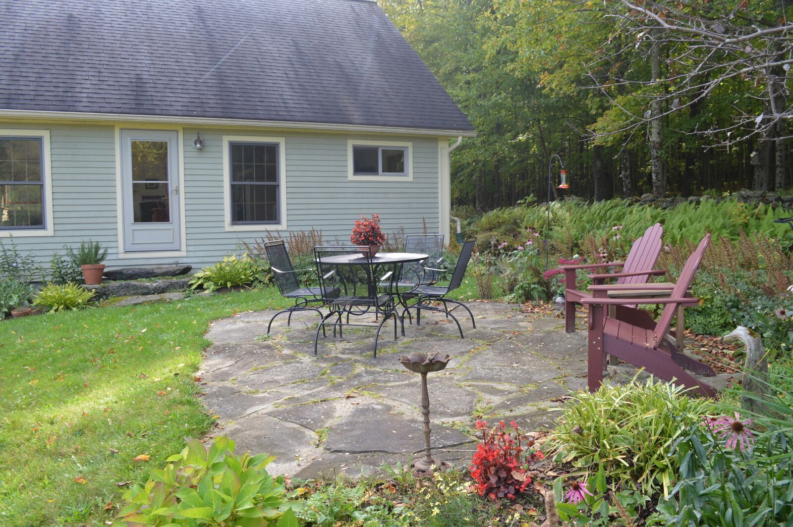 A house with a stone patio, a table with chairs, and a bird feeder.