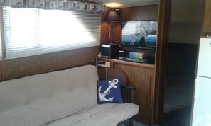 A compact RV interior with a sofa, a television, and a small kitchen area.