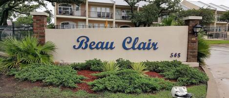 A sign for Beau Clair, a multi-story building with balconies and a brick facade.