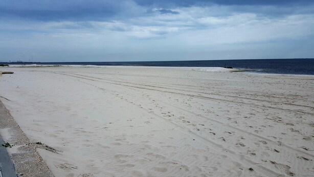 Une vaste plage de sable où l’on peut voir des empreintes de pas qui mènent vers l’océan.