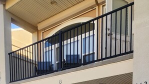 Un immeuble de deux étages doté d’un balcon, portant le numéro 113, et d’un espace d’entrée abrité avec des chaises bleues.