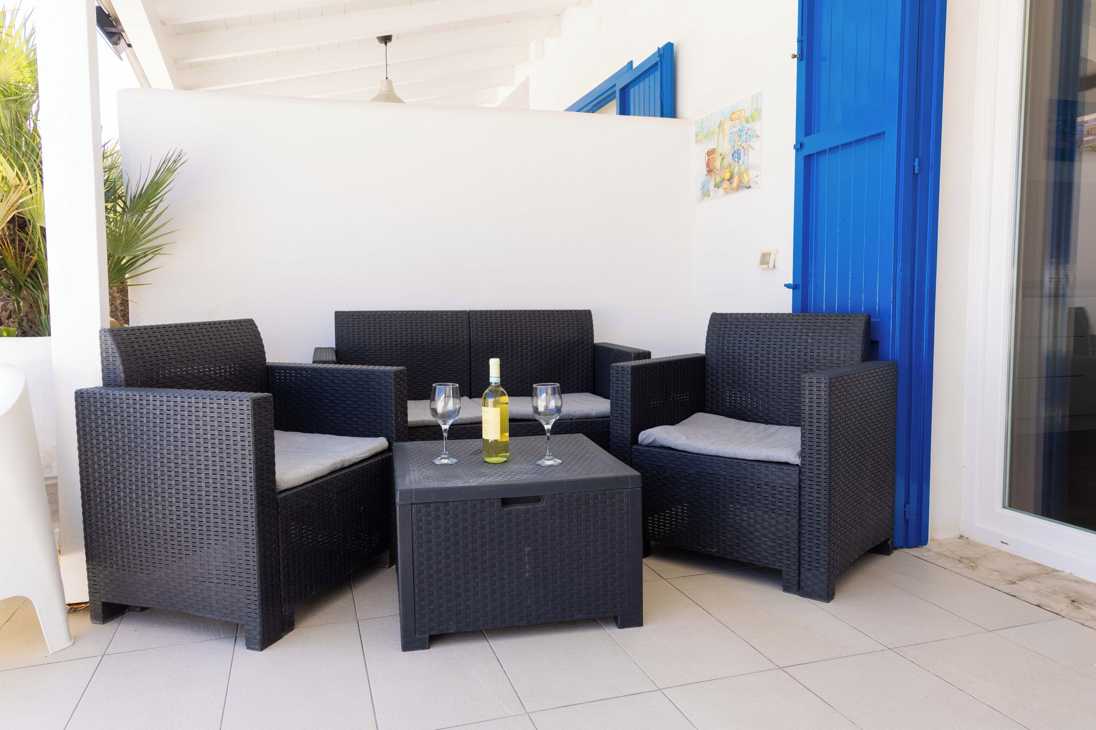 A corner seating area with wicker furniture and a small table, a bottle of wine, and two glasses.