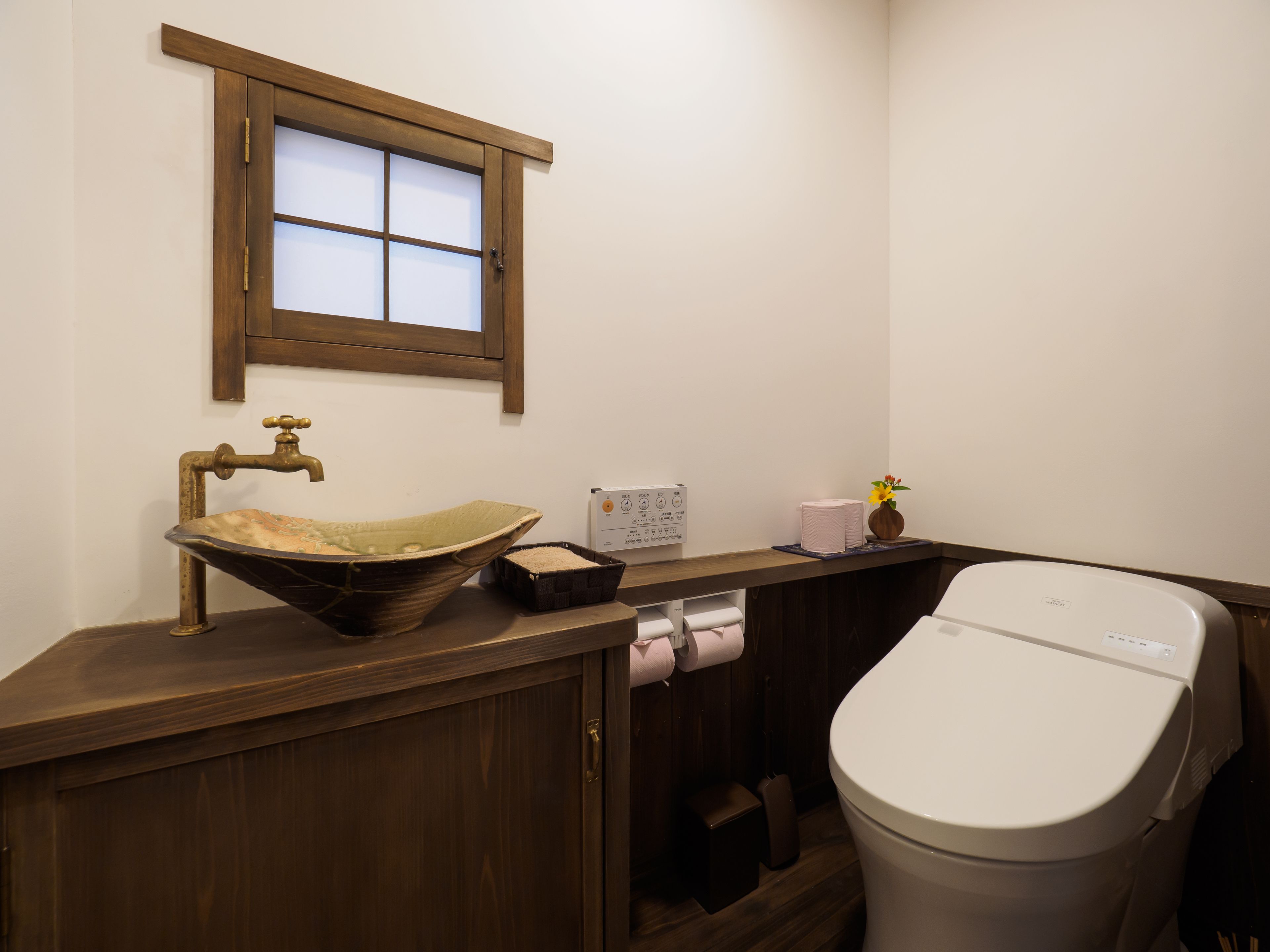 A bathroom with a wooden vanity, a sink with a decorative basin, a toilet, and a window above the sink.