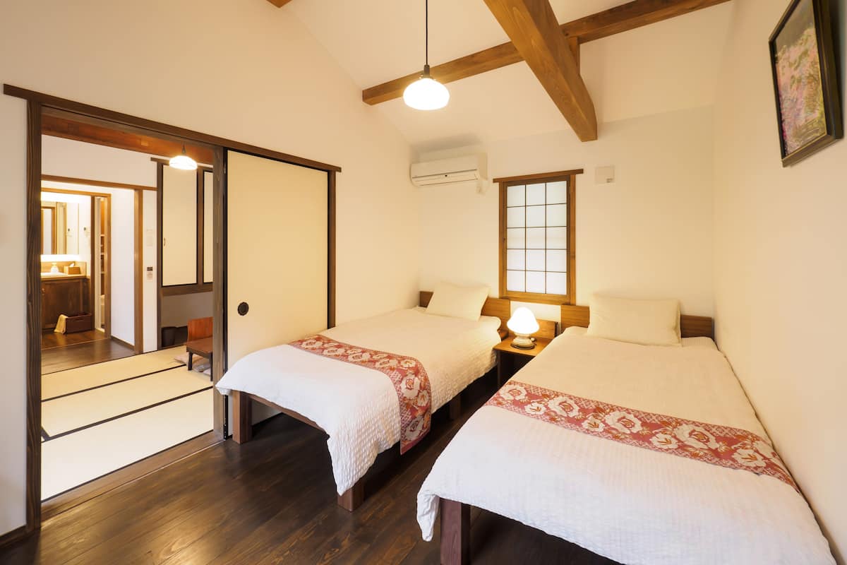 A hotel room with two beds, wooden beams, a large window, and a traditional Japanese sliding door.