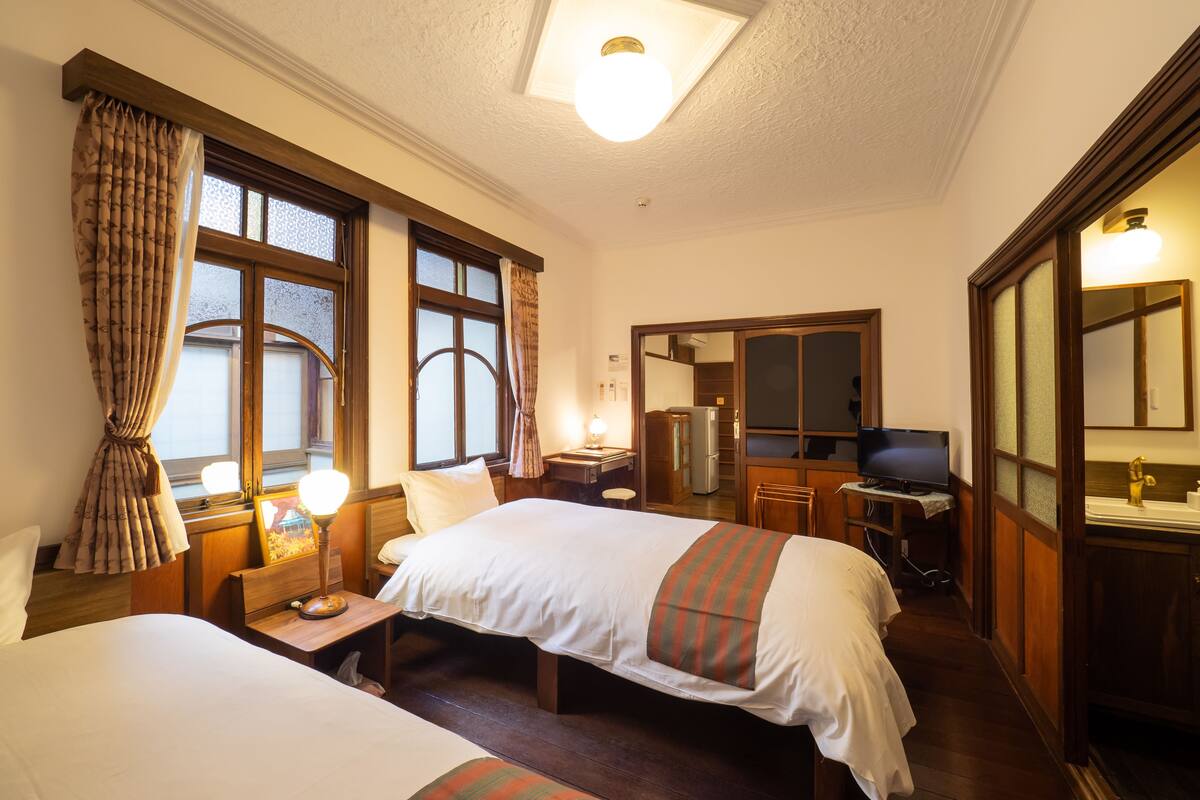 A hotel room with two beds, a desk, a television, and a bathroom.