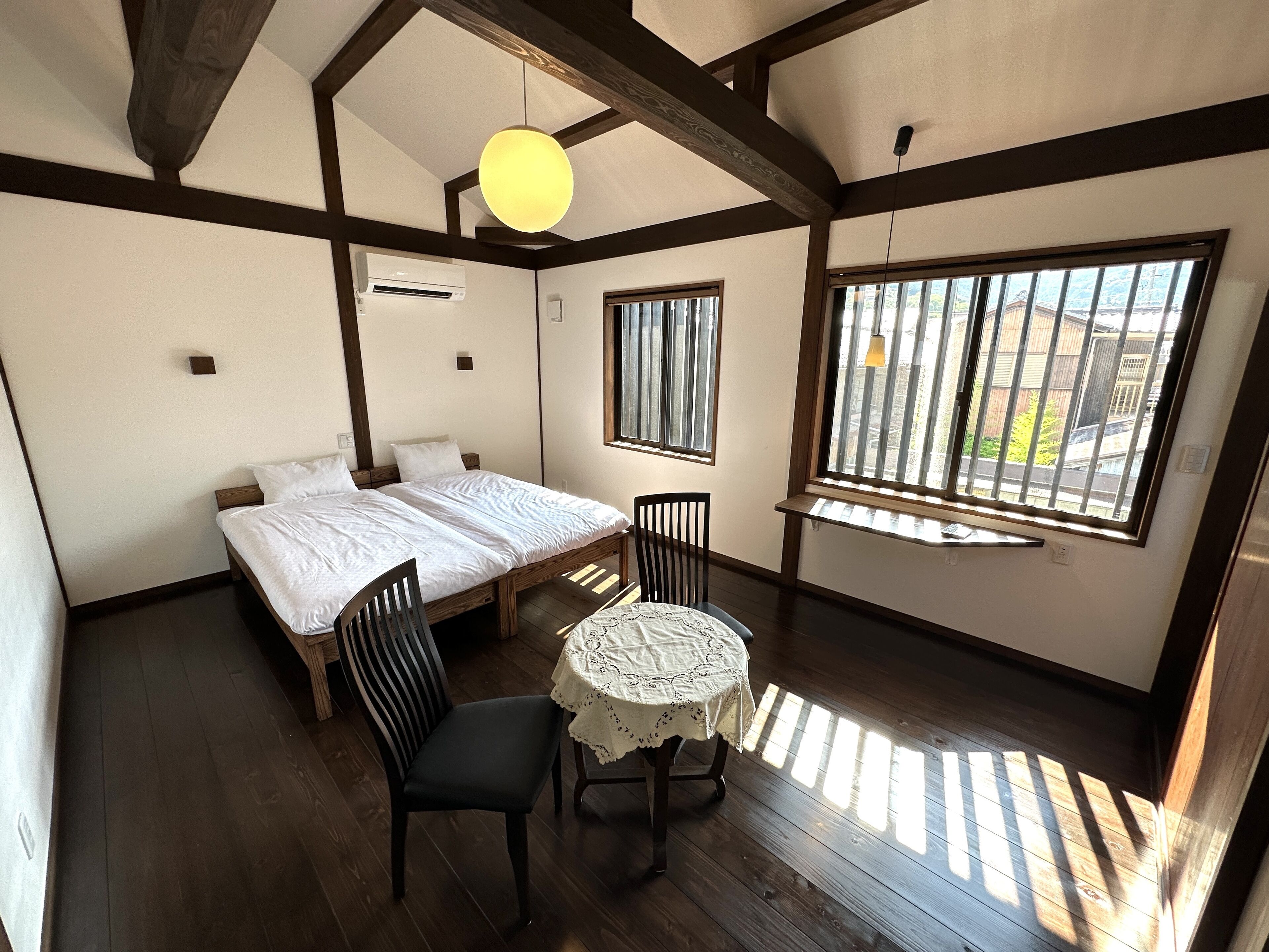 A bedroom with a bed, two chairs, a small table, and a window with bars.