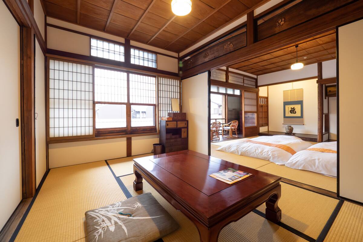 A traditional Japanese room with tatami flooring, a wooden table, a futon bed, and sliding doors.