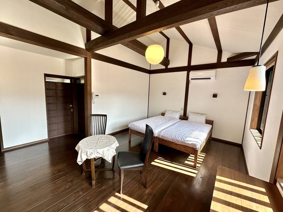 Een kamer met een bed, een tafel met kantkleed, een stoel en een houten vloer.