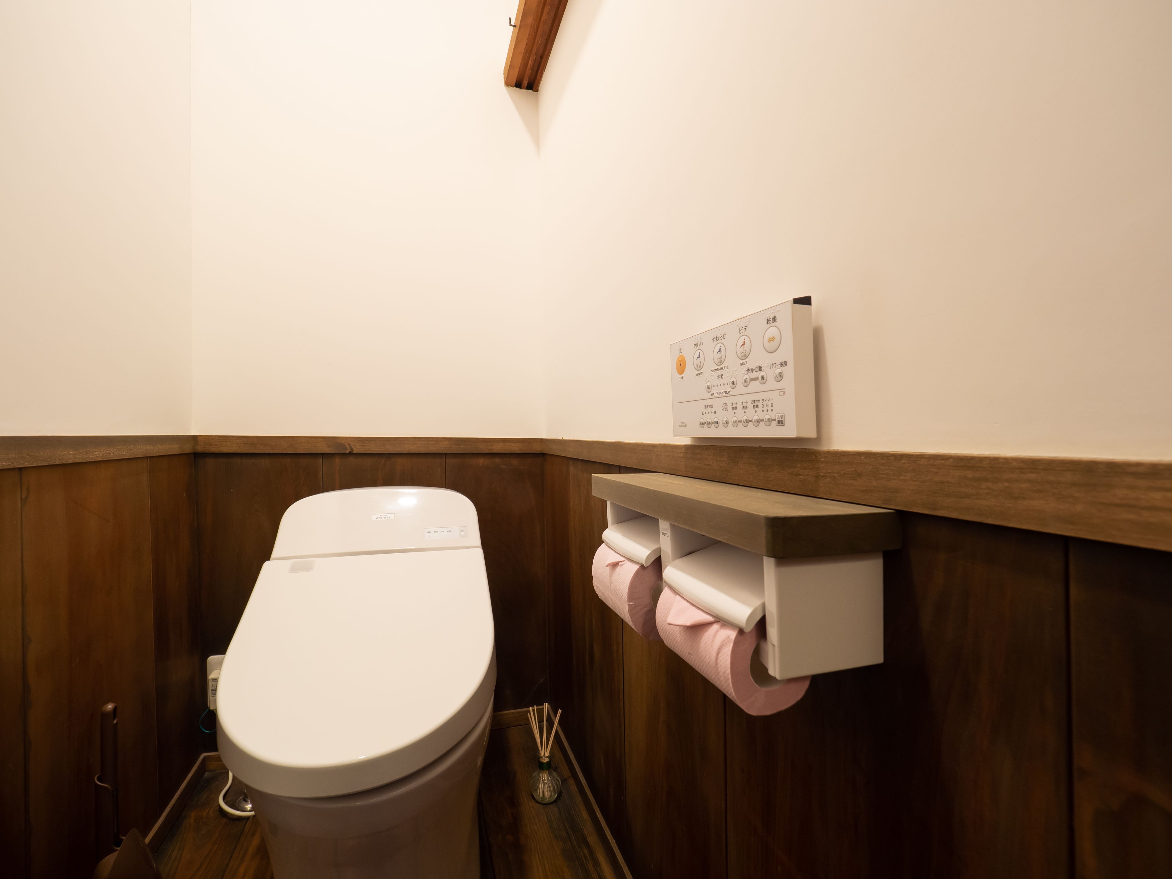 A bathroom with a toilet, a wooden wall, and a control panel above the toilet.