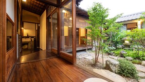 Un intérieur de style japonais traditionnel, avec un plancher en bois, des portes coulissantes et une vue sur un jardin agrémenté de rochers et d’un petit arbre.
