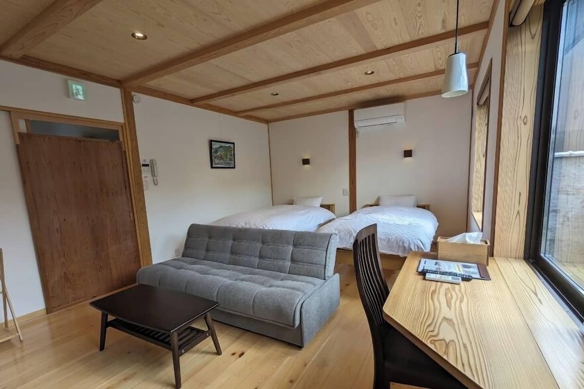 A room with two beds, a sofa, a table, and a window.