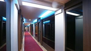 A hotel corridor with a red carpet, modern lighting, and glass doors leading to rooms.