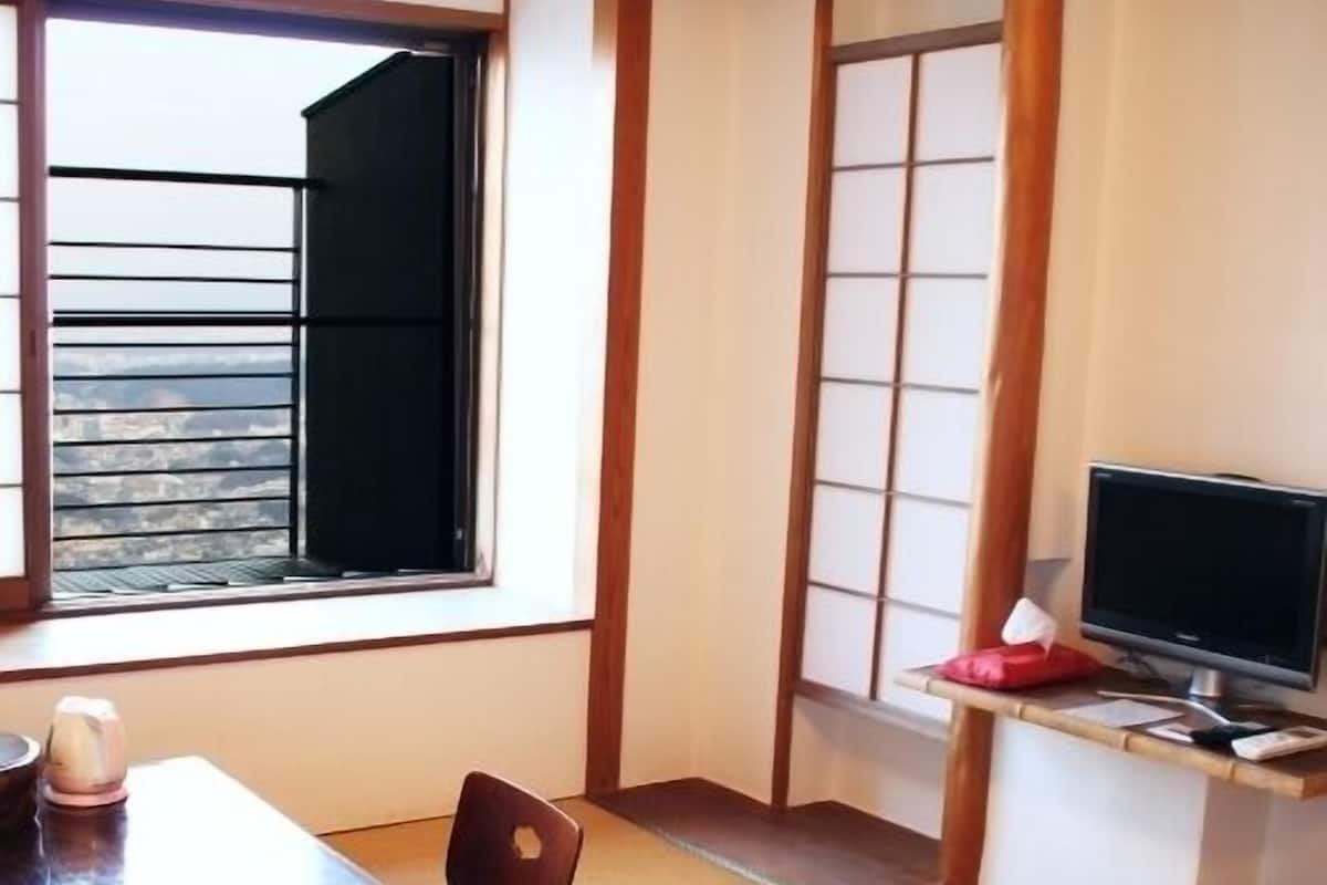 A traditional Japanese room with tatami flooring, a wooden table, a television on a shelf, and a sliding door.