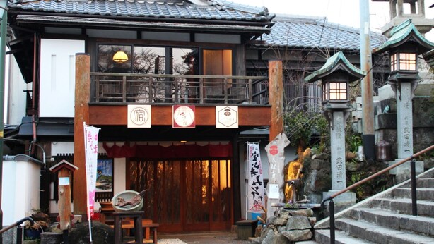 A traditional Japanese building with a wooden facade, a tiled roof, and a stone lantern. - Monzen Okagero (Ikoma)