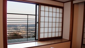 A room with a sliding shoji screen, a view of a cityscape, and a wooden table with a bowl and a pitcher. - Monzen Okagero (Ikoma)