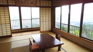 A traditional Japanese room with tatami flooring, a low table, and a view of a cityscape through large windows. - Monzen Okagero (Ikoma)