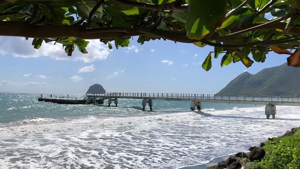 Eine Pier, die sich ins Meer erstreckt, mit einer Bergkulisse im Hintergrund.