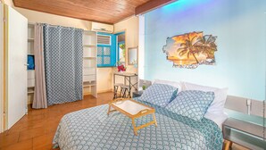 Ein Schlafzimmer mit einem Bett, Holzboden, einer Wand mit einem Sonnenuntergangsgemälde und einem Badezimmer mit Duschvorhang.