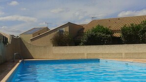 A swimming pool with a tiled deck, surrounded by a low wall and a building with a tiled roof. - Marseillan house without opposite in the peace, garden terrace, in a residence (Marseillan)