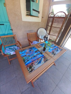 A patio area with a wooden table and chairs, a glass-top table with a printed map, and a view through a window. - Marseillan house without opposite in the peace, garden terrace, in a residence (Marseillan)