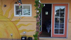 Une maison ornée d’une fresque représentant un soleil, une porte décorée d’une plante et une fenêtre surmontée d’une sculpture d’oiseau.