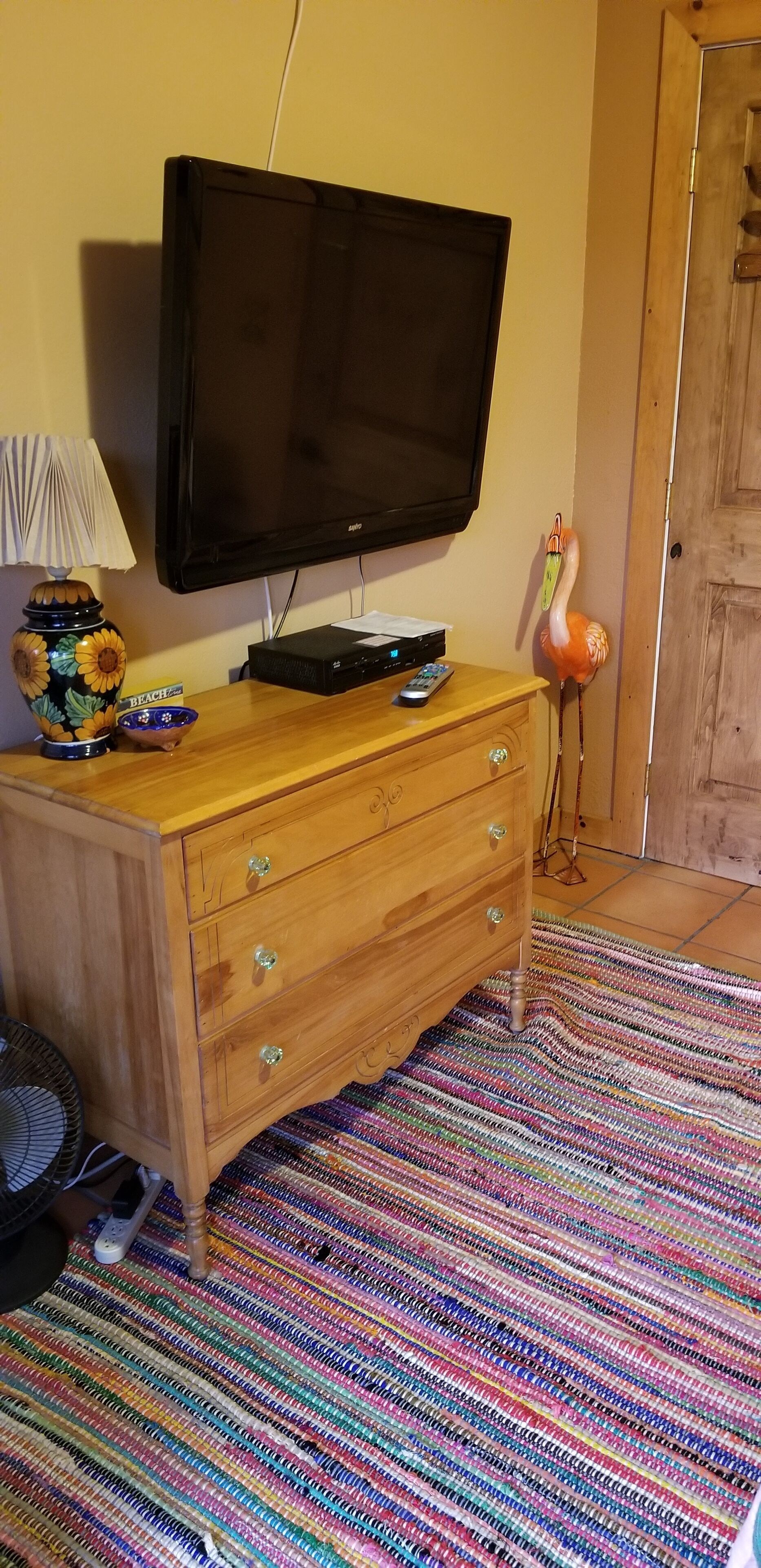 A wooden TV stand with a flat-screen TV, a lamp, and a decorative flamingo.