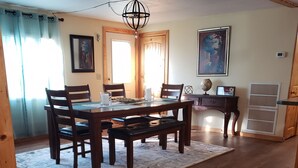 A dining area with a wooden table and chairs, a chandelier, and a large window with curtains.