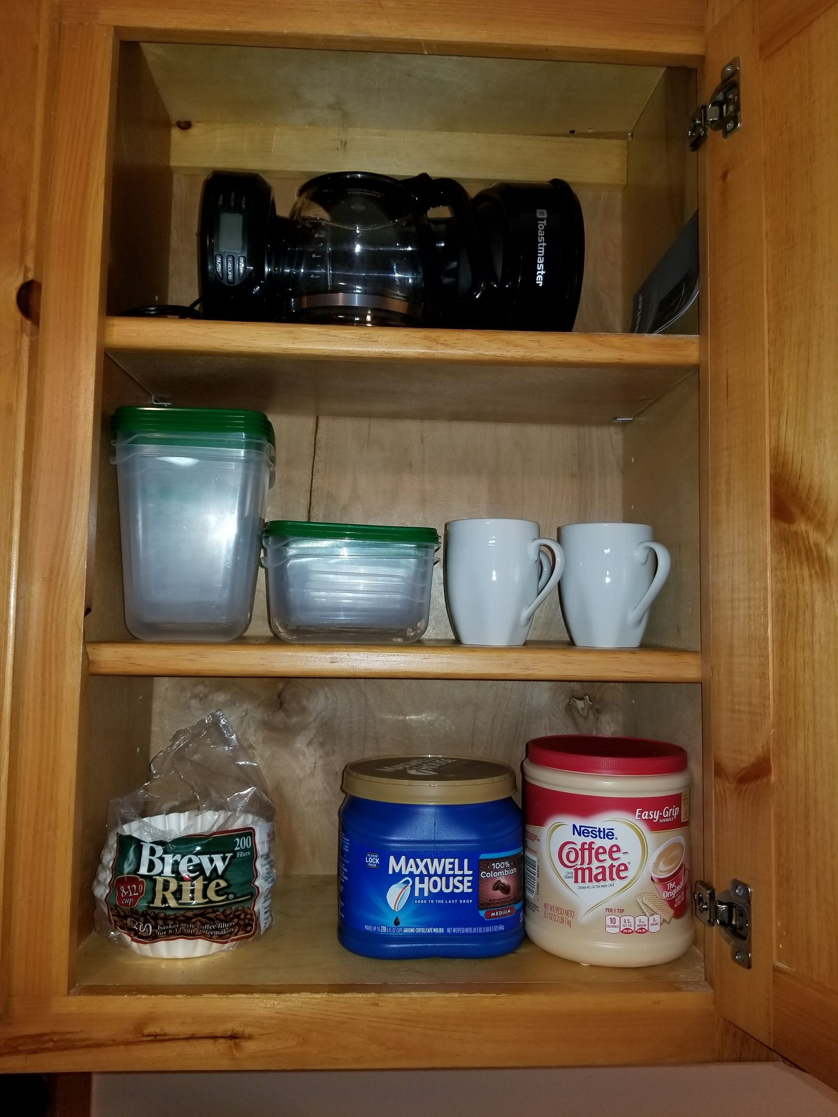 A kitchen cabinet with storage containers, a coffee maker, and a coffee maker on the shelves.