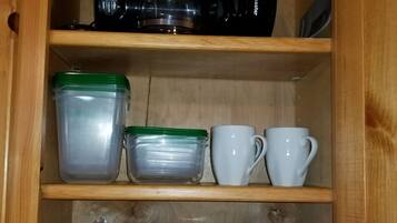 A kitchen cabinet with storage containers, a coffee maker, and a coffee maker on the shelves.