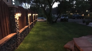 A well-maintained garden with a stone wall and wooden fence, a paved walkway, and a car parked in the background. - Historic Downtown Carriage House (Flagstaff)