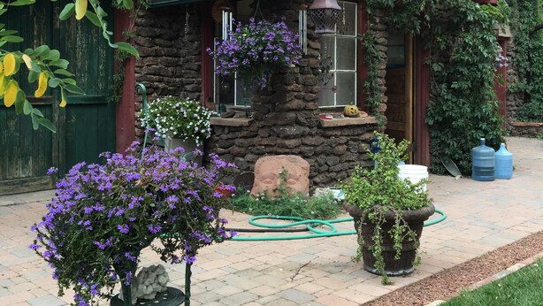 A stone house with a green roof, surrounded by a garden with purple flowers and a lawn. - Historic Downtown Carriage House (Flagstaff)