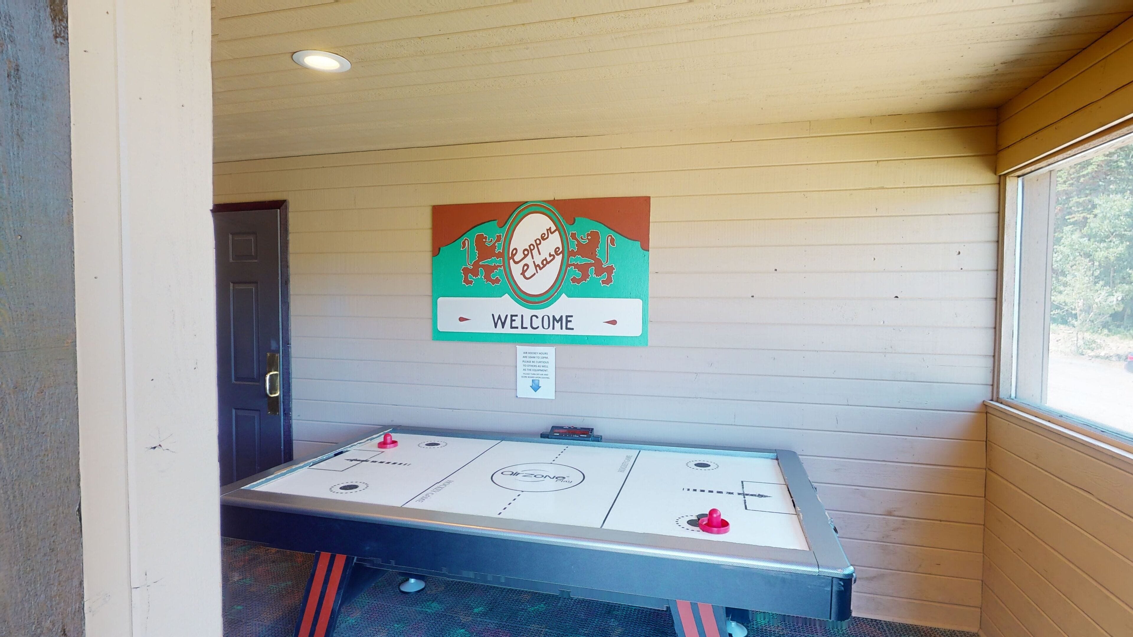 A room with a shuffleboard table, a welcome sign, and a door.