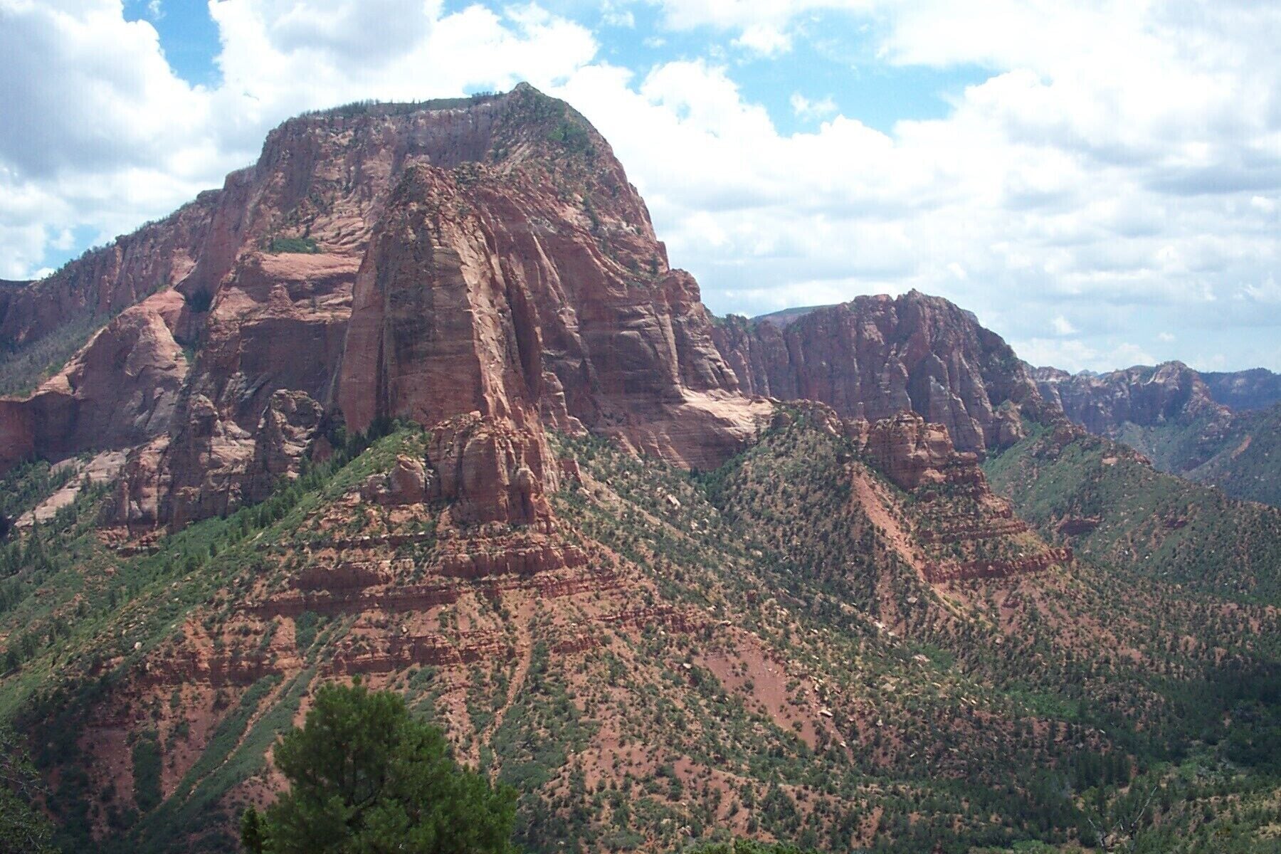 A rugged mountain landscape with a prominent peak and surrounding green vegetation.