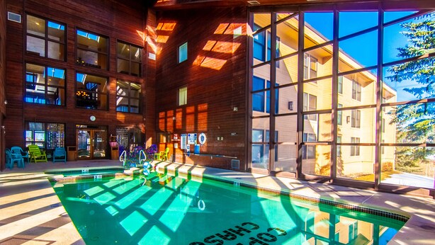 A modern indoor pool with clear glass walls, a wooden exterior, and a view of a neighboring building.
