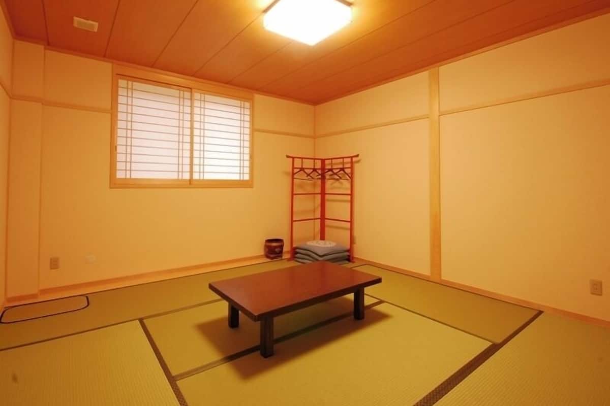 Une pièce de style japonais traditionnel, avec un sol recouvert de tatamis, une basse table en bois, une fenêtre ornée de paravents shoji et un meuble de rangement rouge suspendu.
