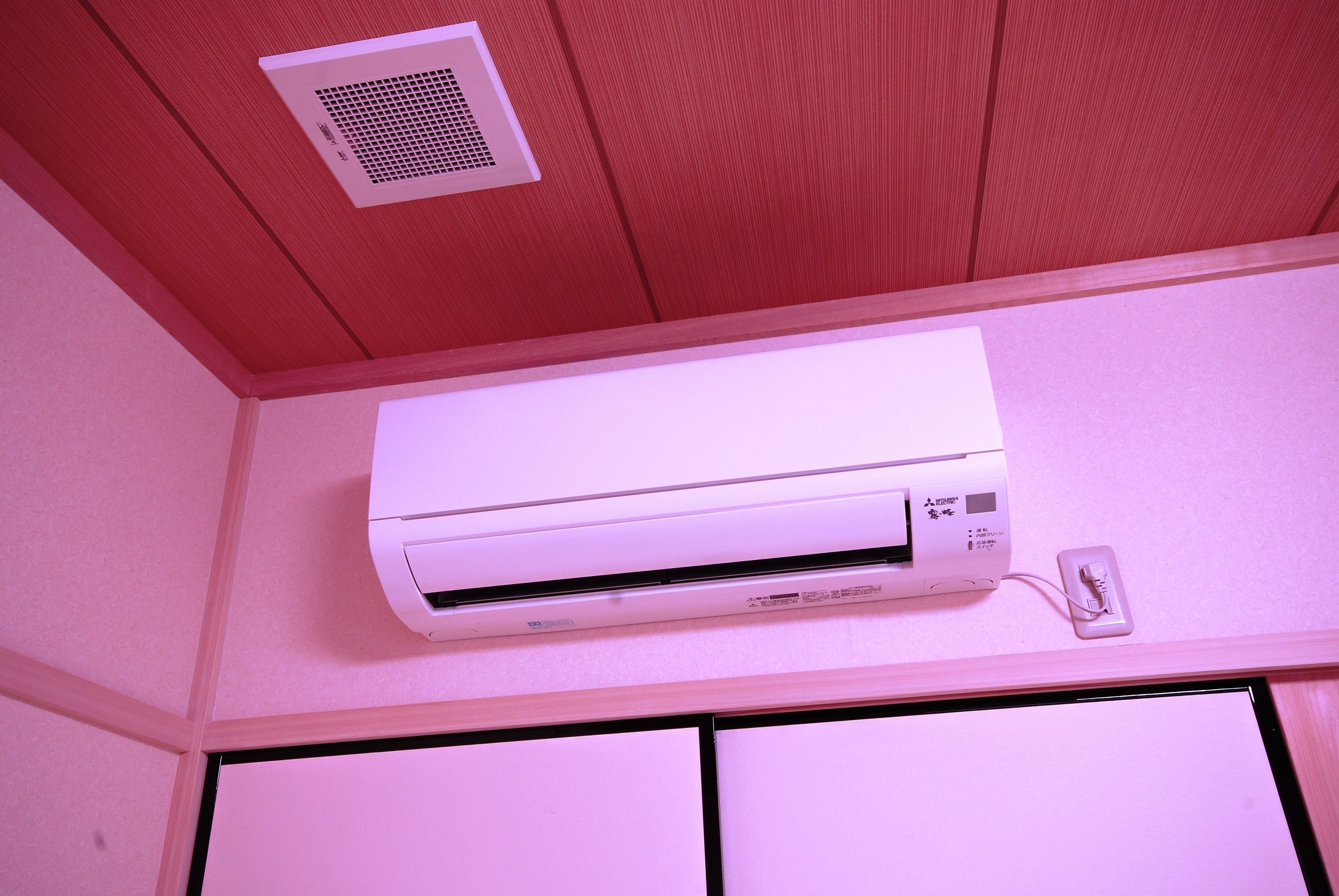 A white air conditioning unit mounted on a wall with a power outlet nearby.