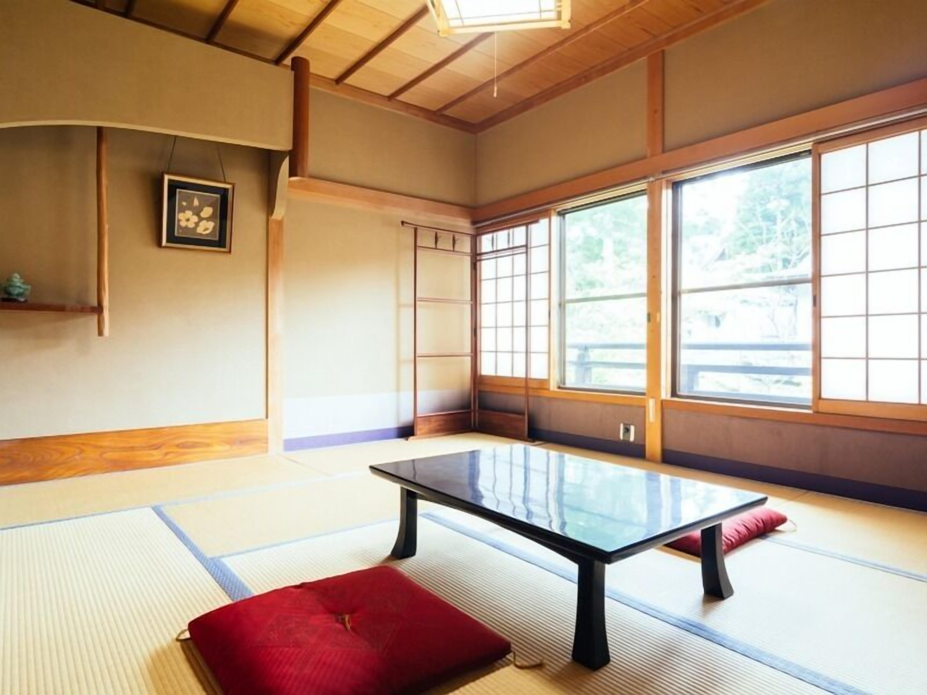 Una habitación con esteras de tatami, una mesa baja, un cojín rojo y un cuadro en la pared.