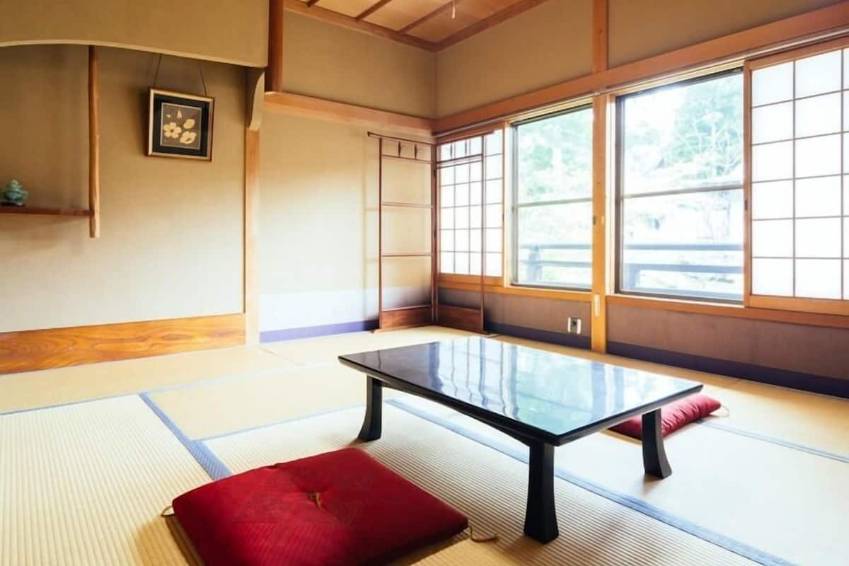 Una habitación con esteras de tatami, una mesa baja, un cojín rojo y un cuadro en la pared.