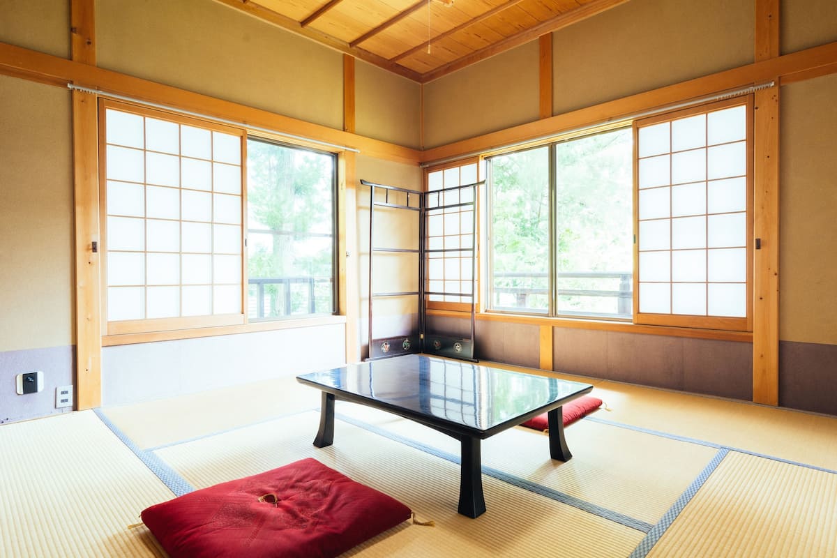 Une pièce avec un sol recouvert de tatamis, une table en tatami, un coussin rouge et des portes coulissantes.