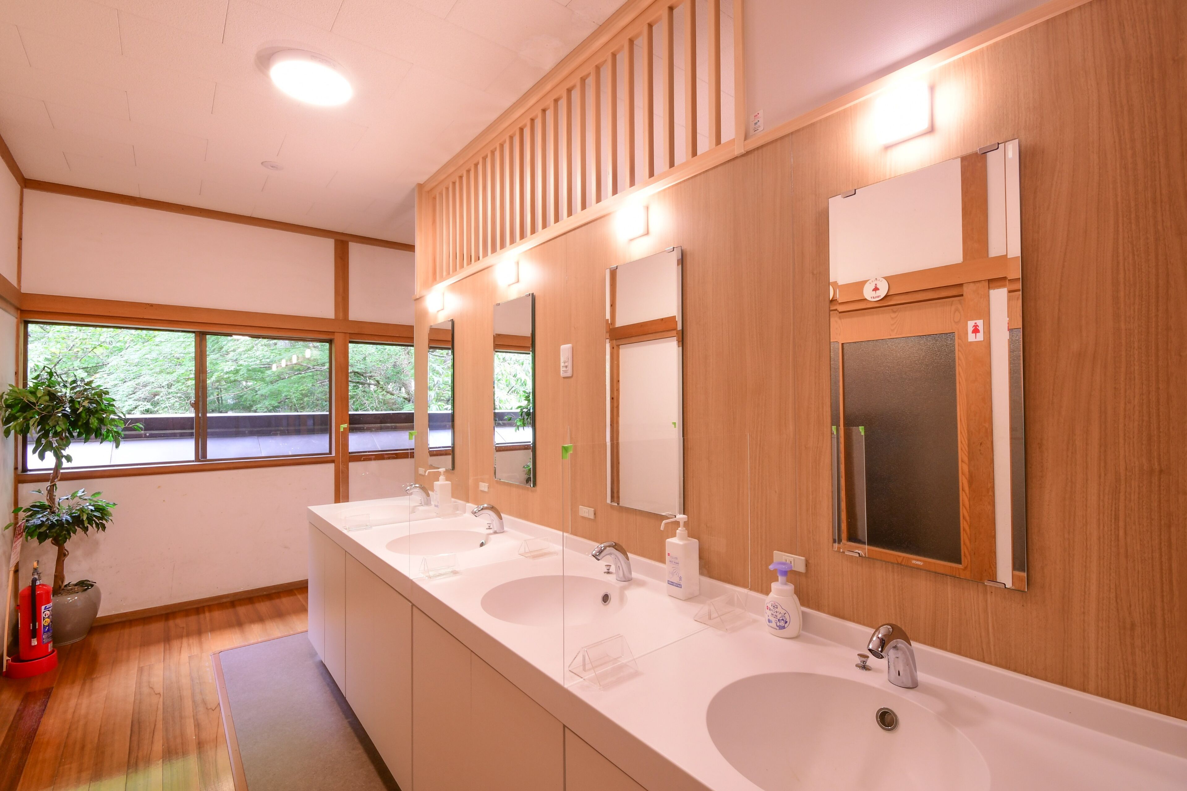 Ein modernes Badezimmer mit drei Waschbecken, Holzvertäfelung und großen Fenstern.