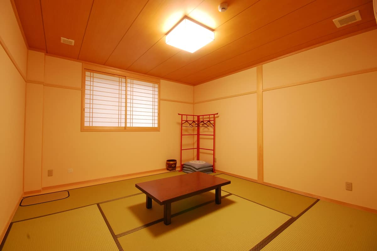 Une pièce de style japonais traditionnel, avec un sol recouvert de tatamis, une basse table en bois, une fenêtre ornée de paravents shoji et un paravent rouge pliant.
