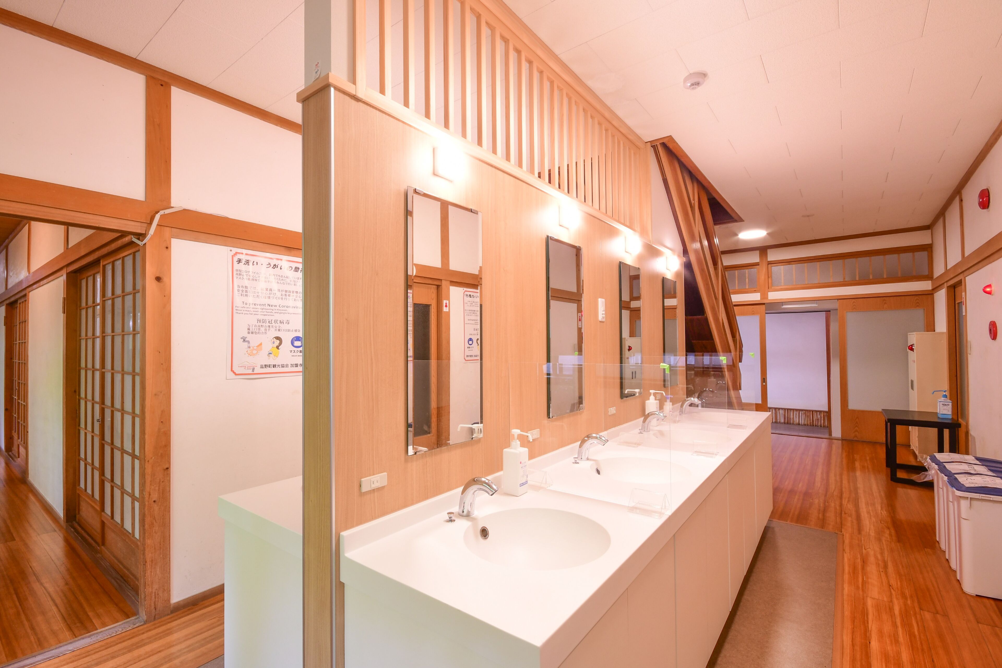 A hotel bathroom with three sinks, wooden paneling, and a staircase.